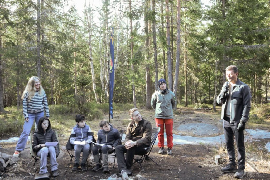 Fylkesråd Lars Monsen snakker i mikrofon. Fire elever, forfatter Håkon Marcus og to representanter fra fylkeskommunen hører på. De befinner seg i skogen.