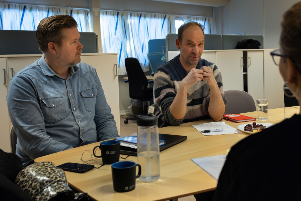 Tre personer sitter ved et bord og snakker sammen