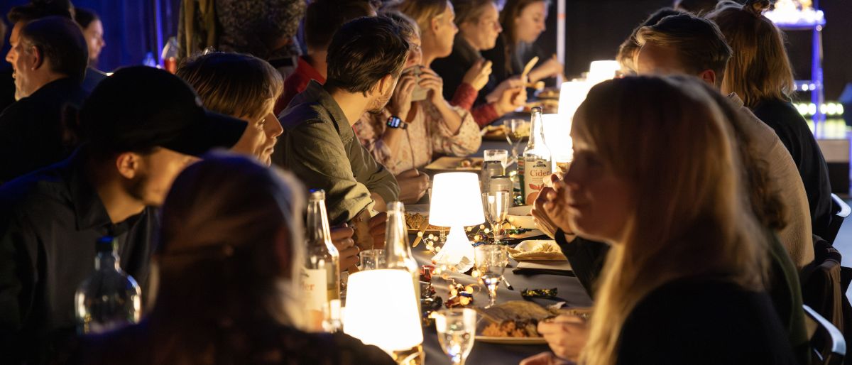 Flere mennesker som sitter ved et langbord og spiser.