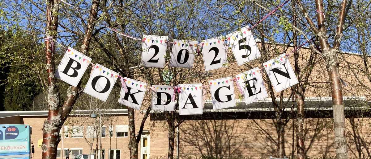Bilde av et banner som er hengt opp i trærne med teksten "2025 Bokdagen"