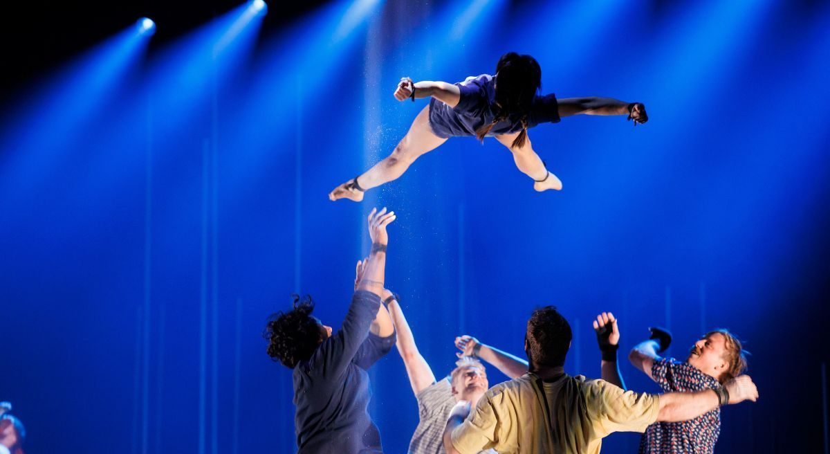 En person kastes i været av en gruppe person, badet i scenelys. Foto.