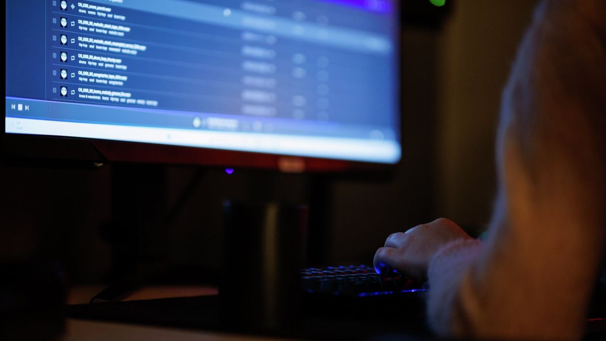 Nærbilde av en datamaskin. Man ser en person sitte foran skjermen.