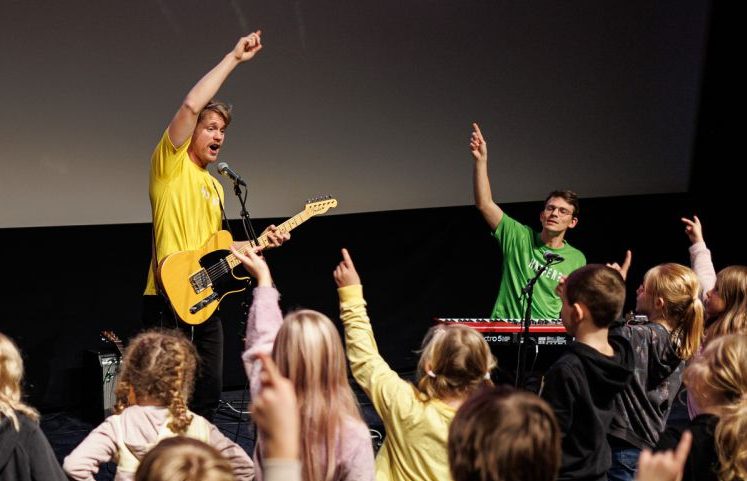 Musikerem med instrumenter holder armen i været foran en gruppe elever. Foto.