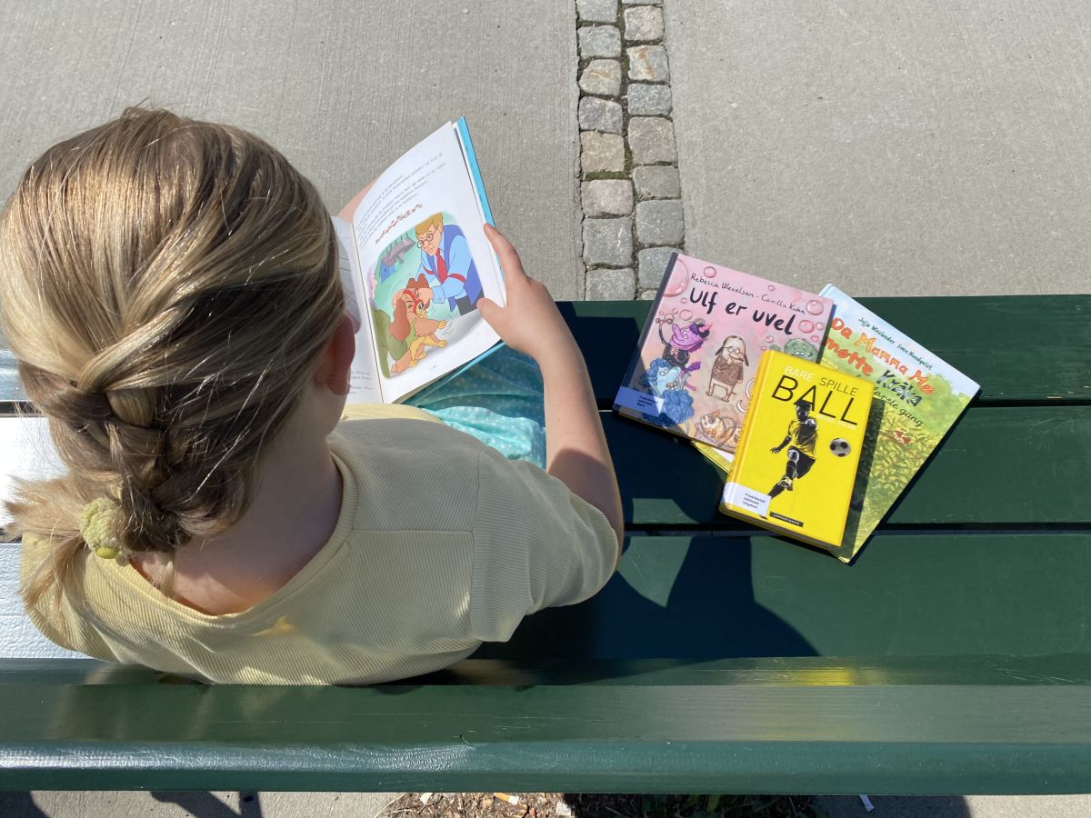 Jente sitter på benk og leser bøker.